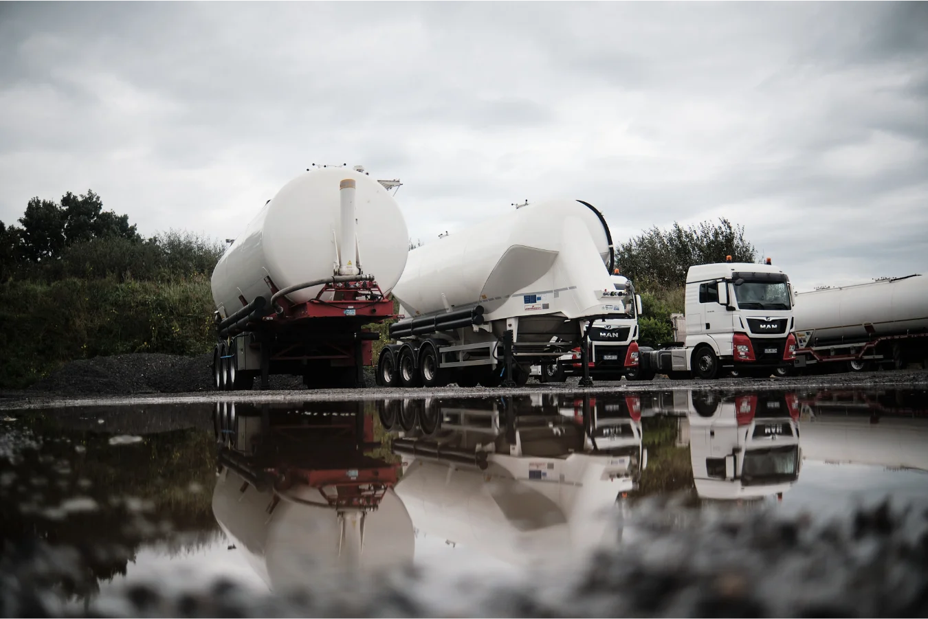 Drei Transporter mit runden Tanks, die sich in einer Pfütze spiegeln